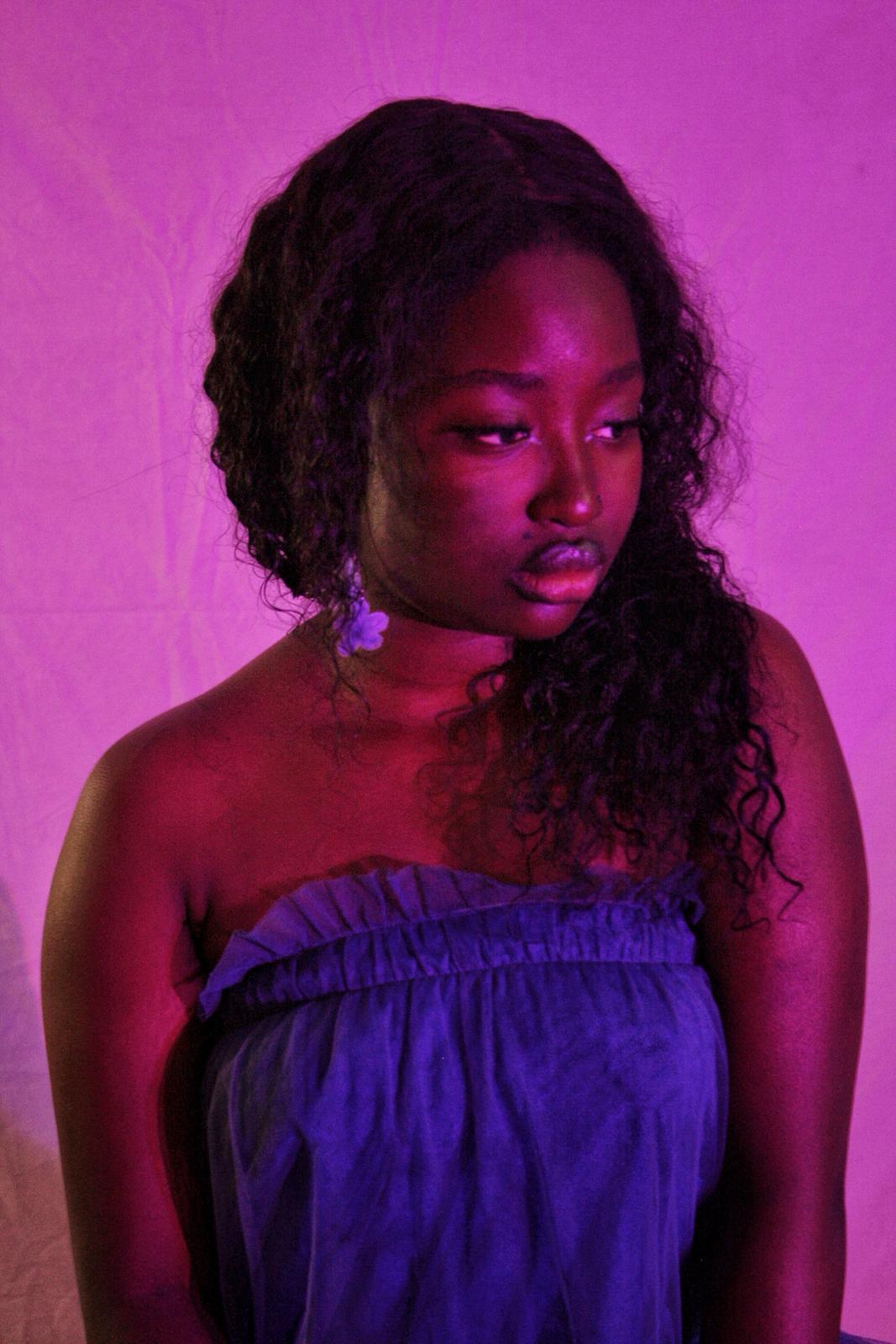 Fatsani in violet light with a flower tucked at her shoulder